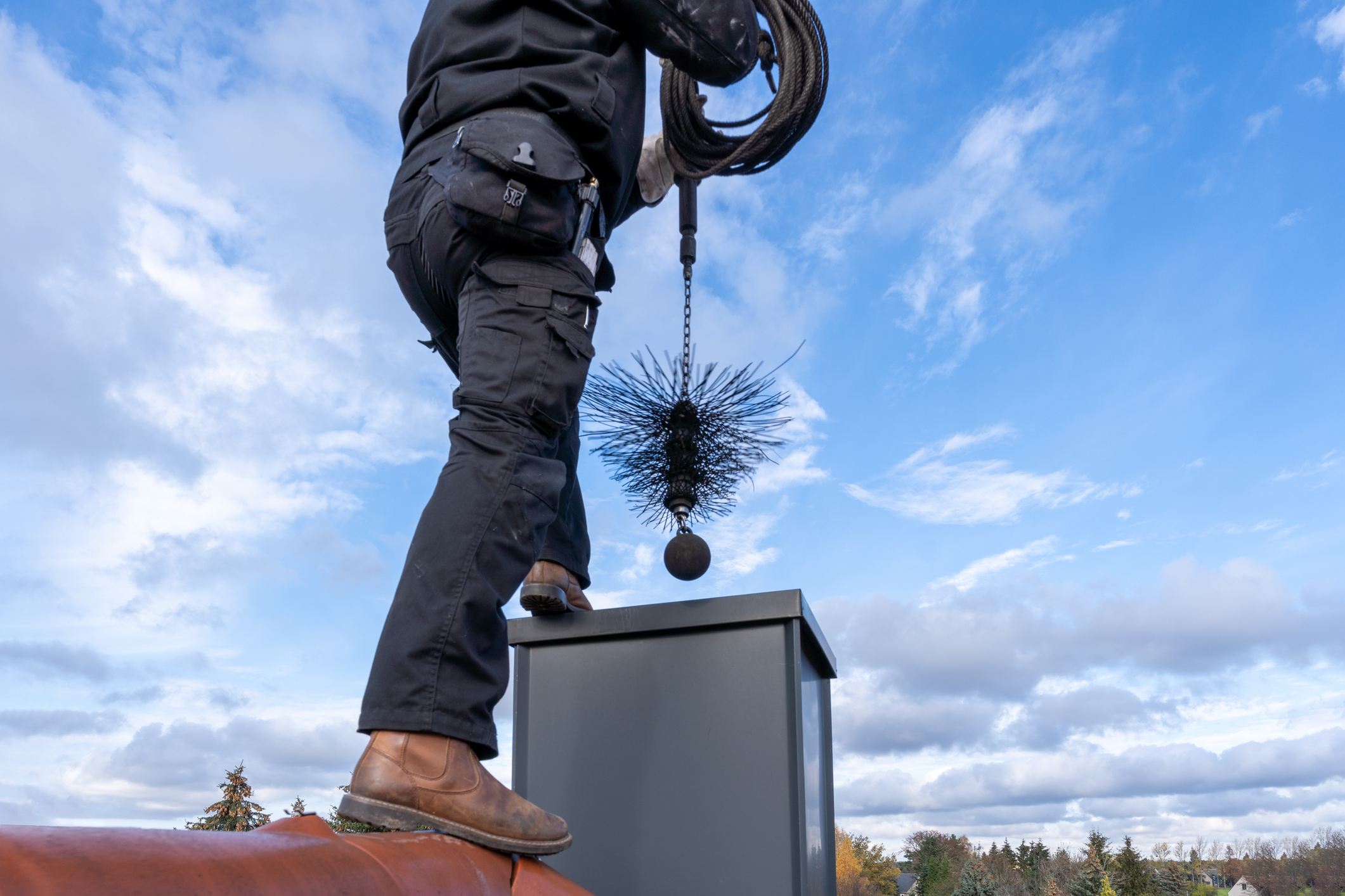 Chimney sweep cleaning a chimney standing on the house roof, lowering equipment down the flue